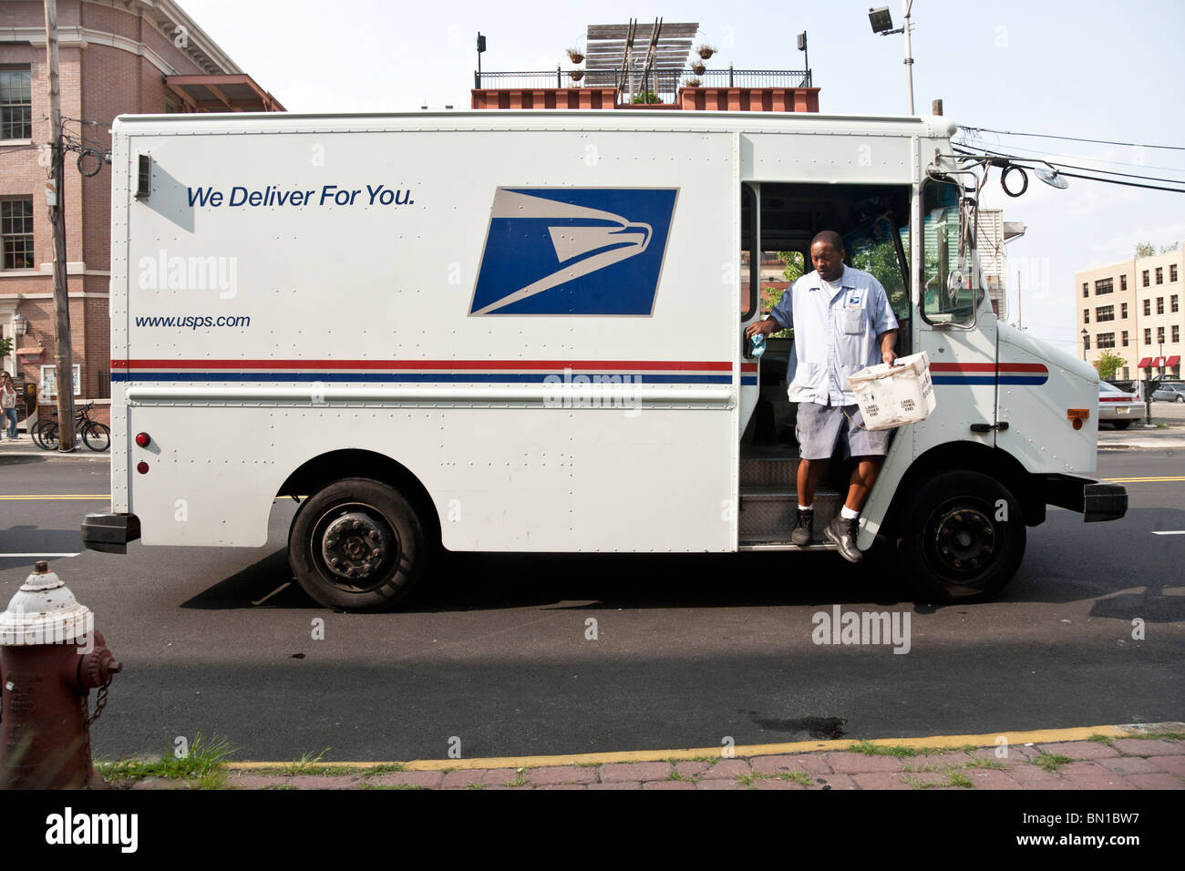 black mail carrier steps down onto street from United States Postal Service delivery truck in uptown Hoboken New Jersey Stock Photo