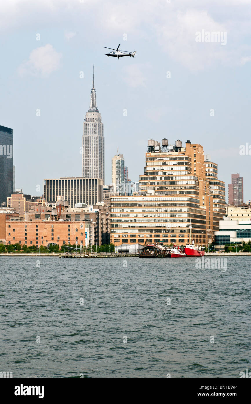 low flying helicopter above Hudson river against water view Manhattan skyline including Empire State & Starrett Lehigh building Stock Photo