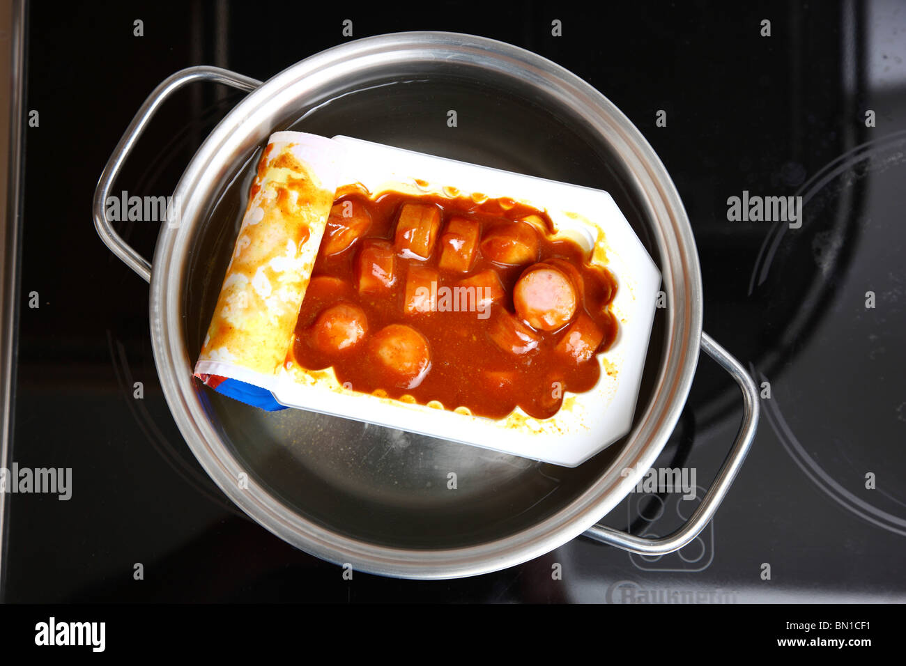 Heating of ready-to-serve meals in hot water. Soups or pasta dishes in cans. Convenience food products. Sausage in tomato sauce. Stock Photo