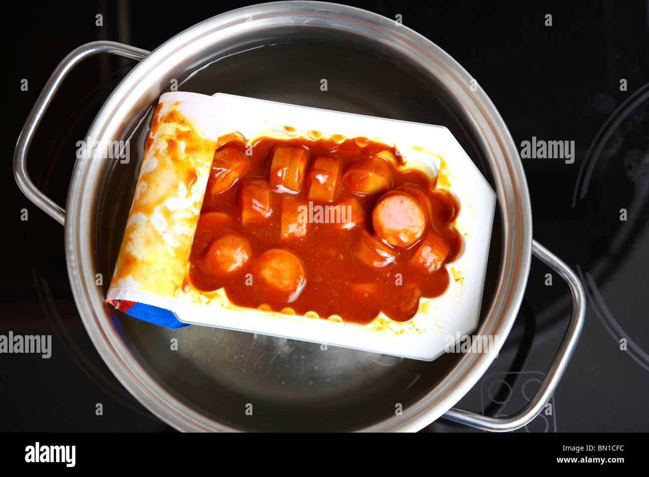 Heating of ready-to-serve meals in hot water. Soups or pasta dishes in cans. Convenience food products. Sausage in tomato sauce Stock Photo