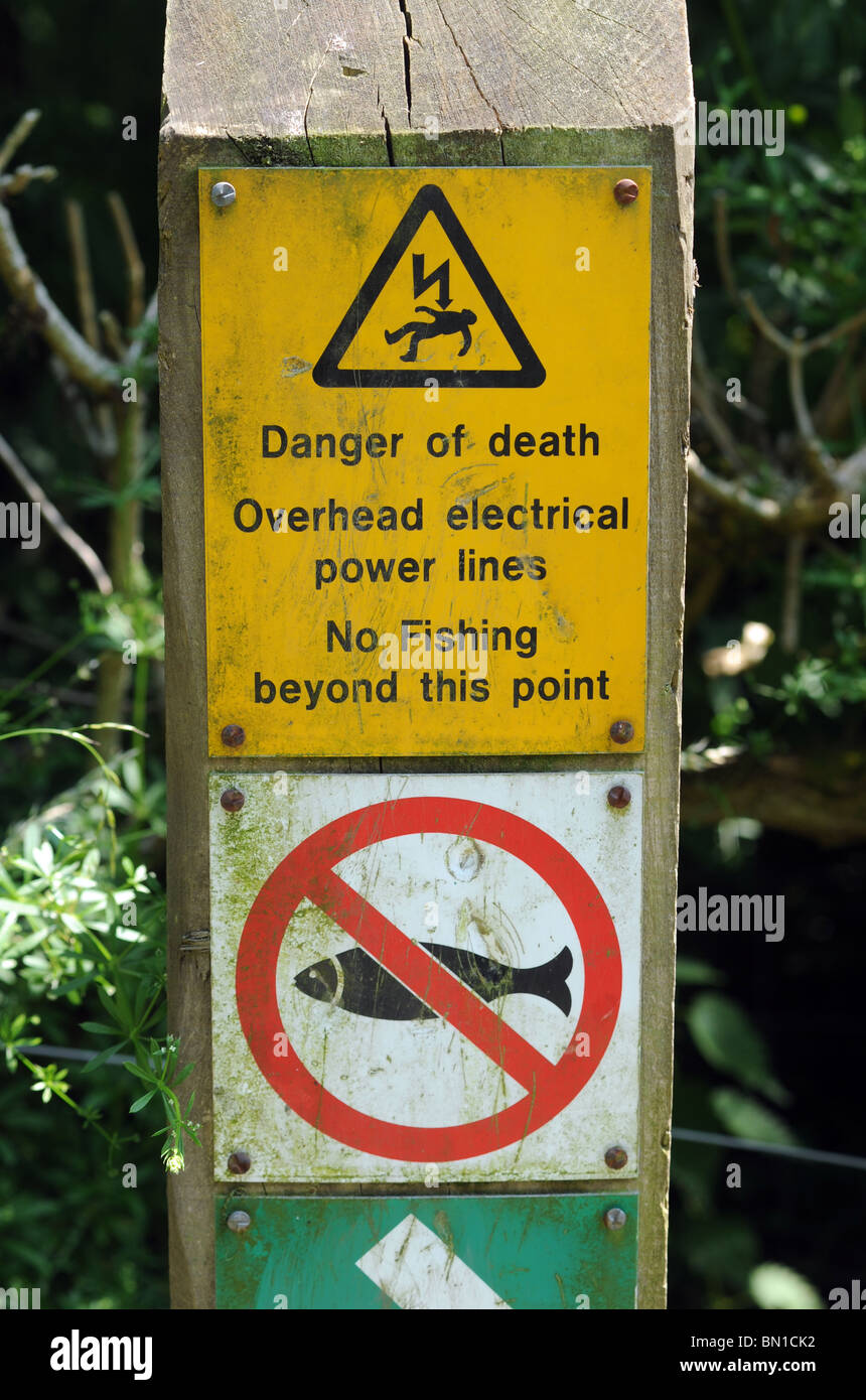 DANGER OF DEATH WARNING SIGNS FOR FISHERMAN BECAUSE OF OVERHEAD ELECTRICAL POWER LINES ON A BRITISH CANAL TOWPATH Stock Photo