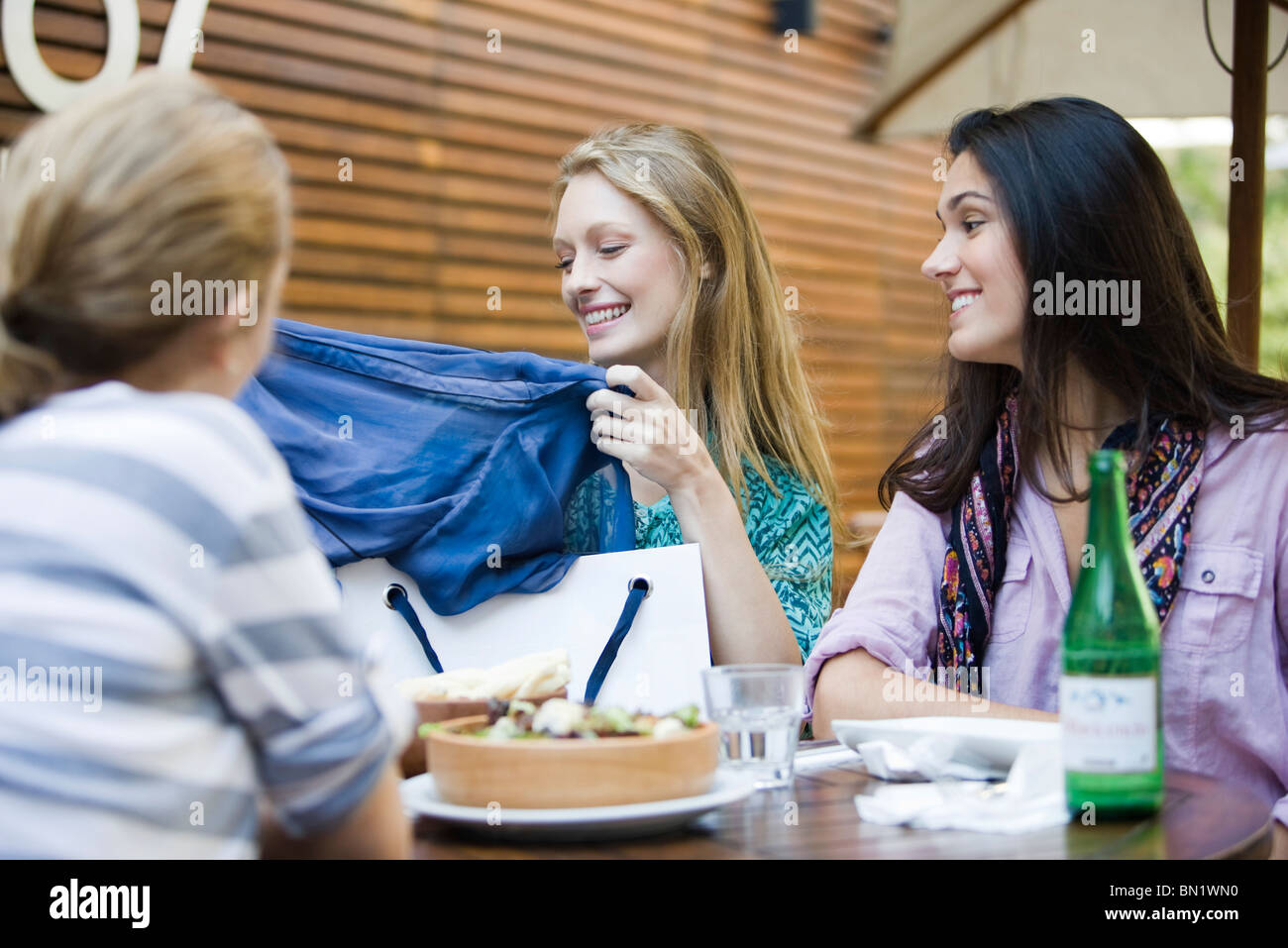 Friends having lunch together in outdoor cafe, one woman showing new clothing in shopping bag Stock Photo