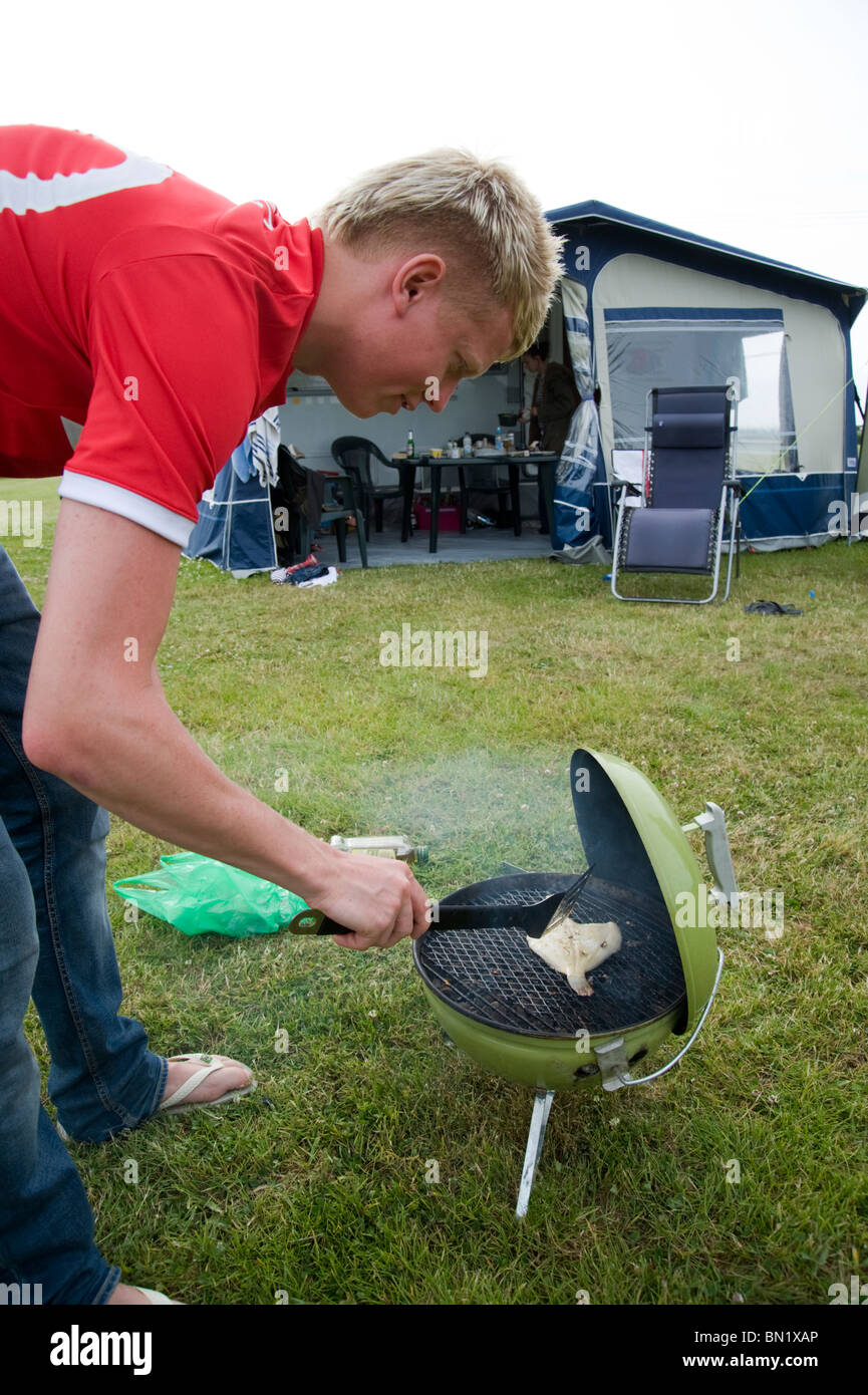 Young man cooking fish on a barbeque while camping and carvanning in Cornwall Stock Photo