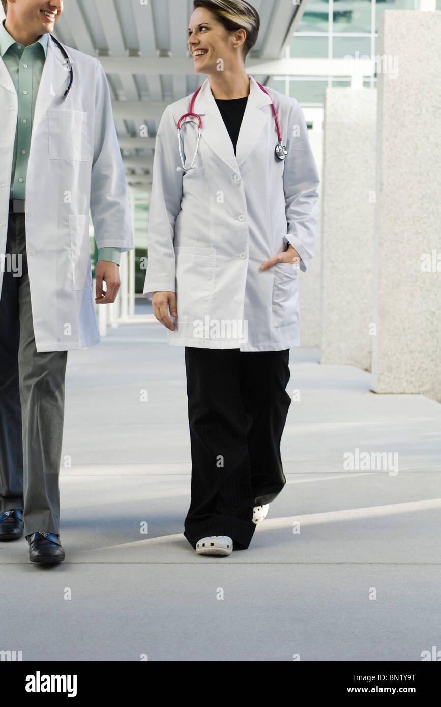 Female doctor walking with colleague along hospital corridor Stock Photo