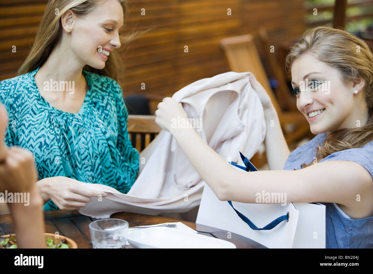 Friends together in outdoor cafe, one woman showing new clothing in shopping bag Stock Photo