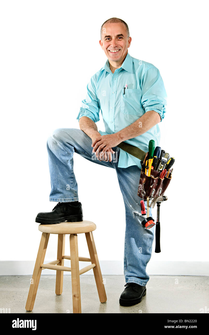 Portrait of smiling handyman with tool belt and stool Stock Photo