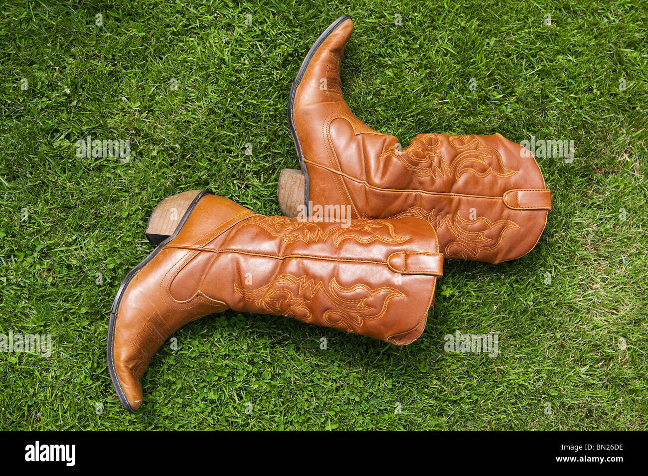 A pair of worn tan leather ladies' cowboy boots lying on the grass, UK Stock Photo