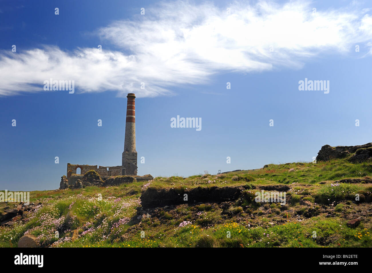 An old chimney of a Cornish tin mine looks like it is still smoking with a passing cloud Stock Photo