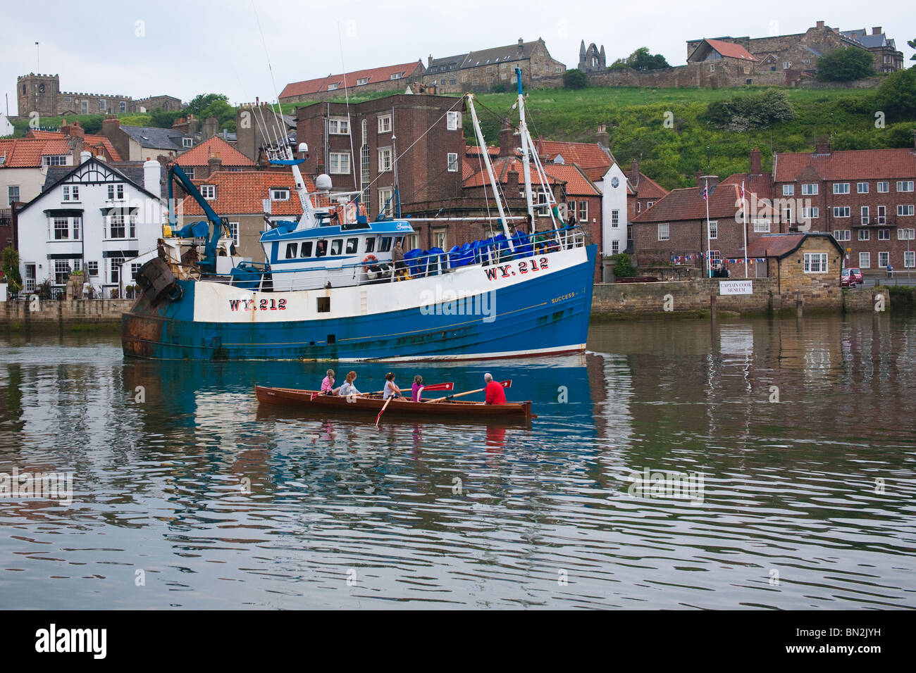 Fishing vessel arriving on the River Esk and passing a small boat full of rowers in Whitby North