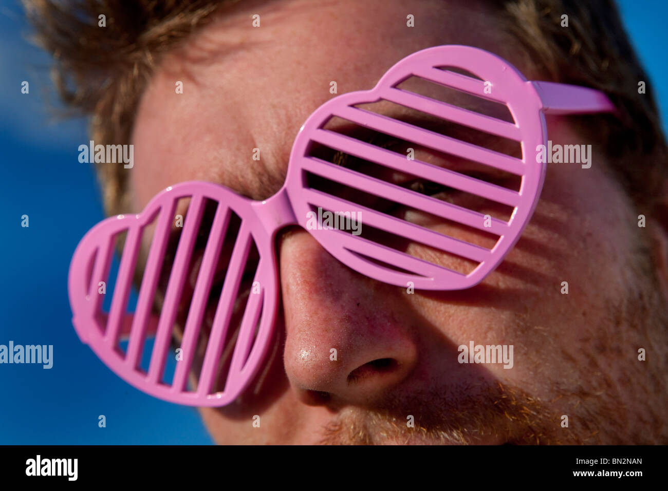 Man wearing pink heart shaped shades at Glastonbury Festival, UK Stock Photo