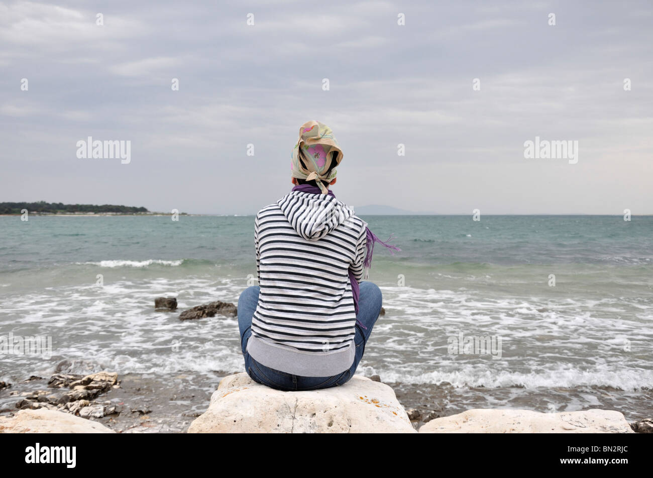 Woman sitting on rocks looking at ocean, rear view Stock Photo - Alamy