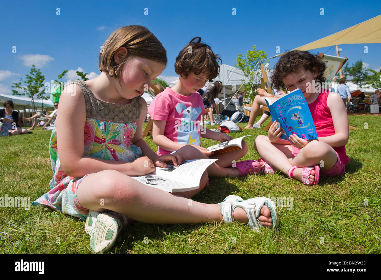 Three young girls sitting on the grass reading books in the summer sunshine at Hay Festival 2010 Hay on Wye Powys Wales UK Stock Photo