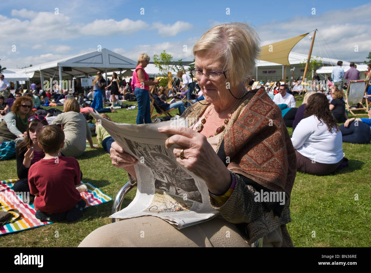 Senior lady amongst crowds reading newspaper in the summer sunshine at Hay Festival 2010 Hay on Wye Powys Wales UK Stock Photo