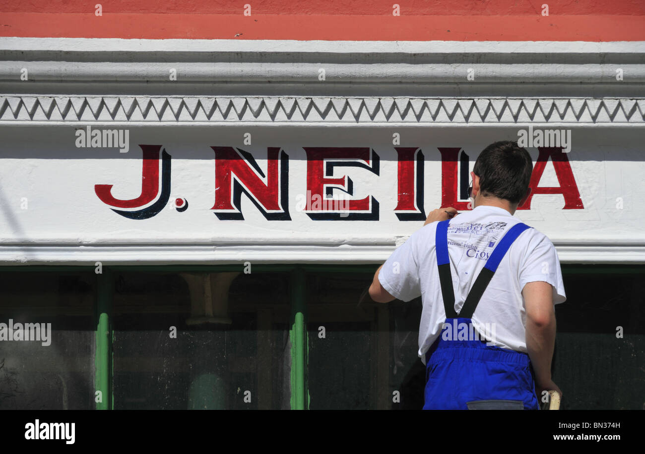 A Sign writer at work on a shop front in County Limerick, Rep of Ireland. Stock Photo