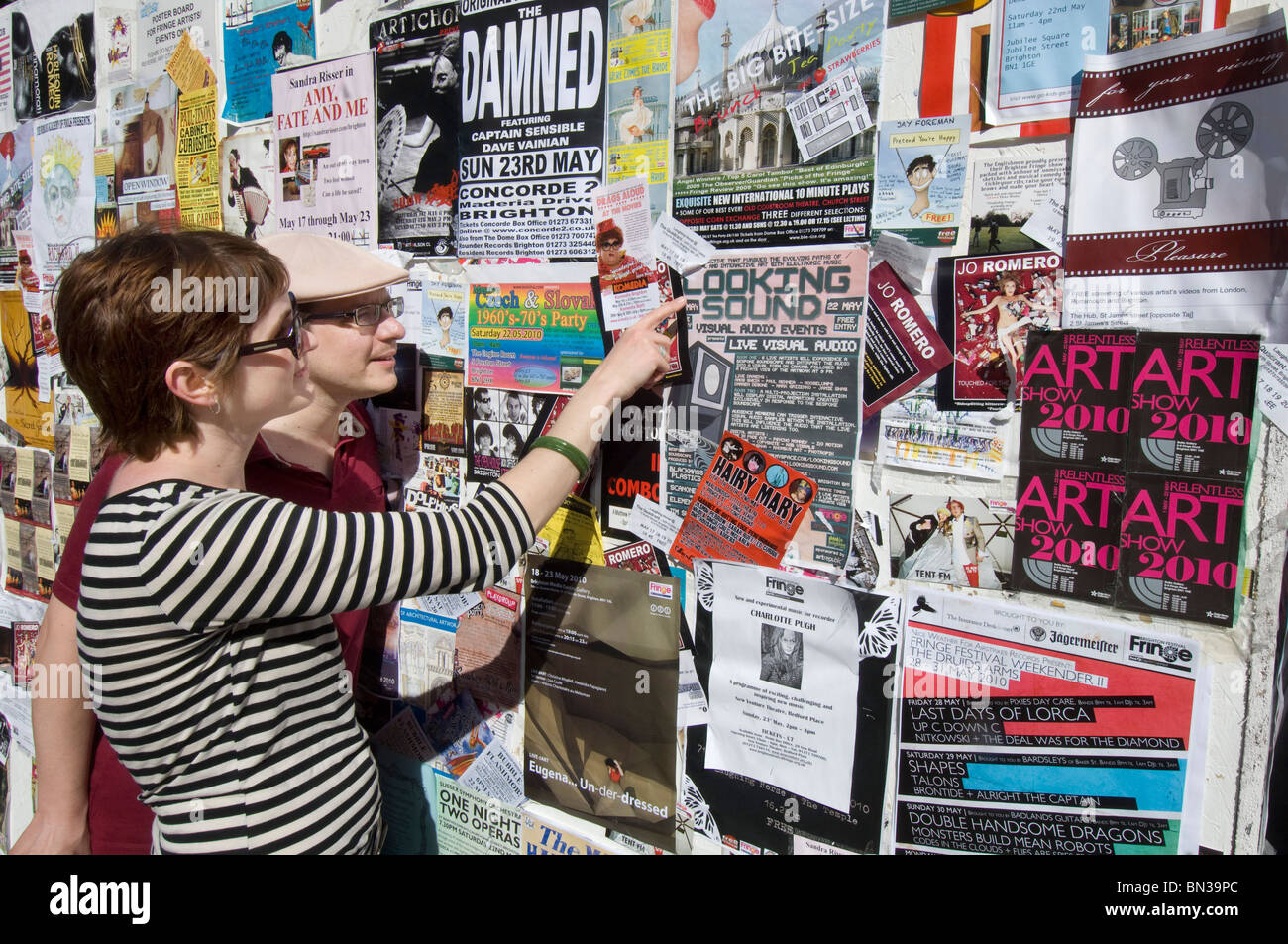 Two festival goers looking at a wall covered with fliers for bands, theatre, art and other Brighton Festival 2010 events Stock Photo