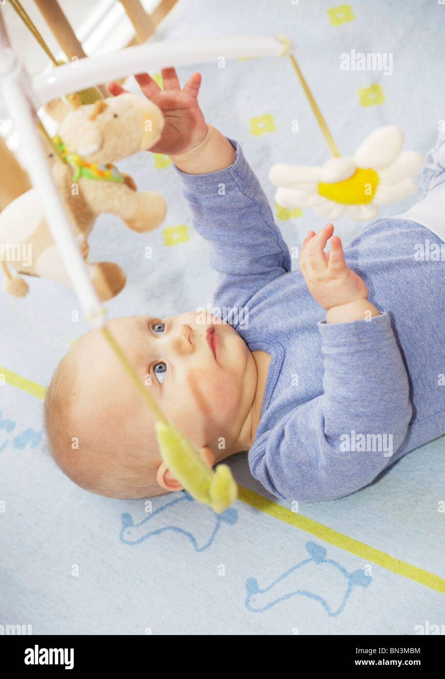 Baby lying in cot and reaching for hanging toys, elevated view Stock