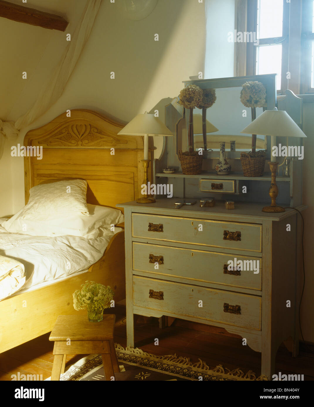 Single pine bed beside blue painted chestofdrawers in small cottage