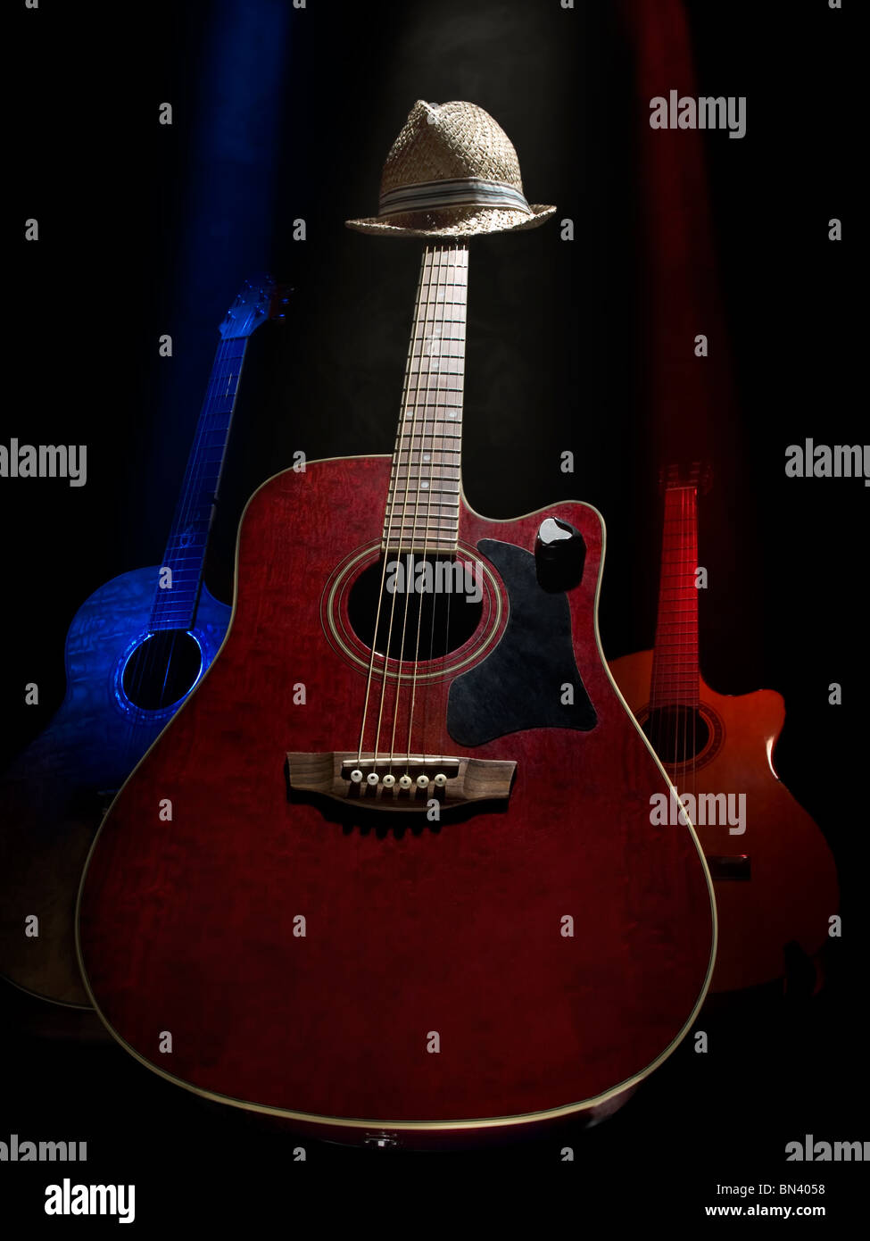 Three acoustic guitars on the stage lit with the overhead lights , against black background, useful for music and entertainment Stock Photo