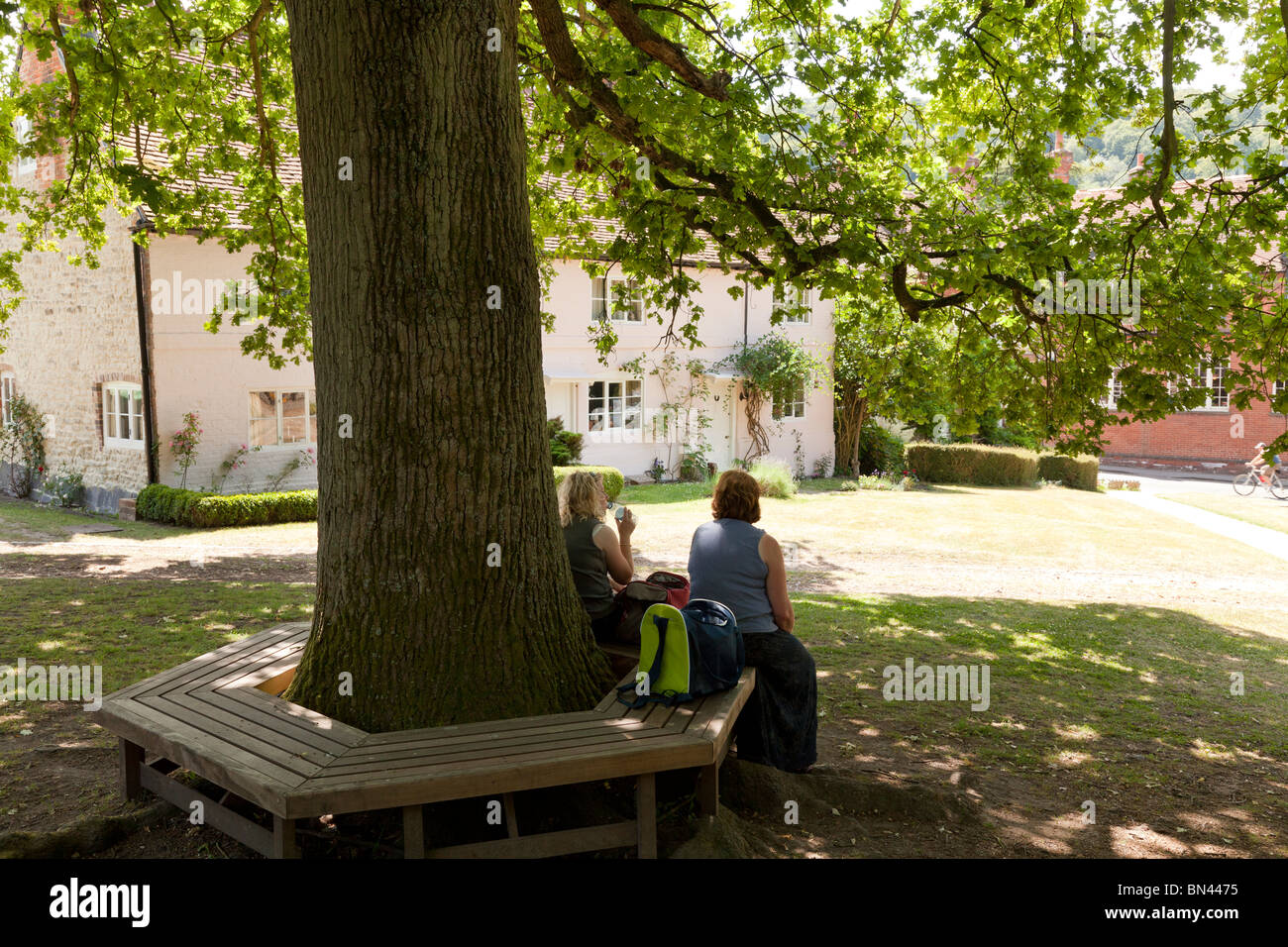 people resting on tree bench under the shade of an oak tree in Selborne outside the church Stock Photo