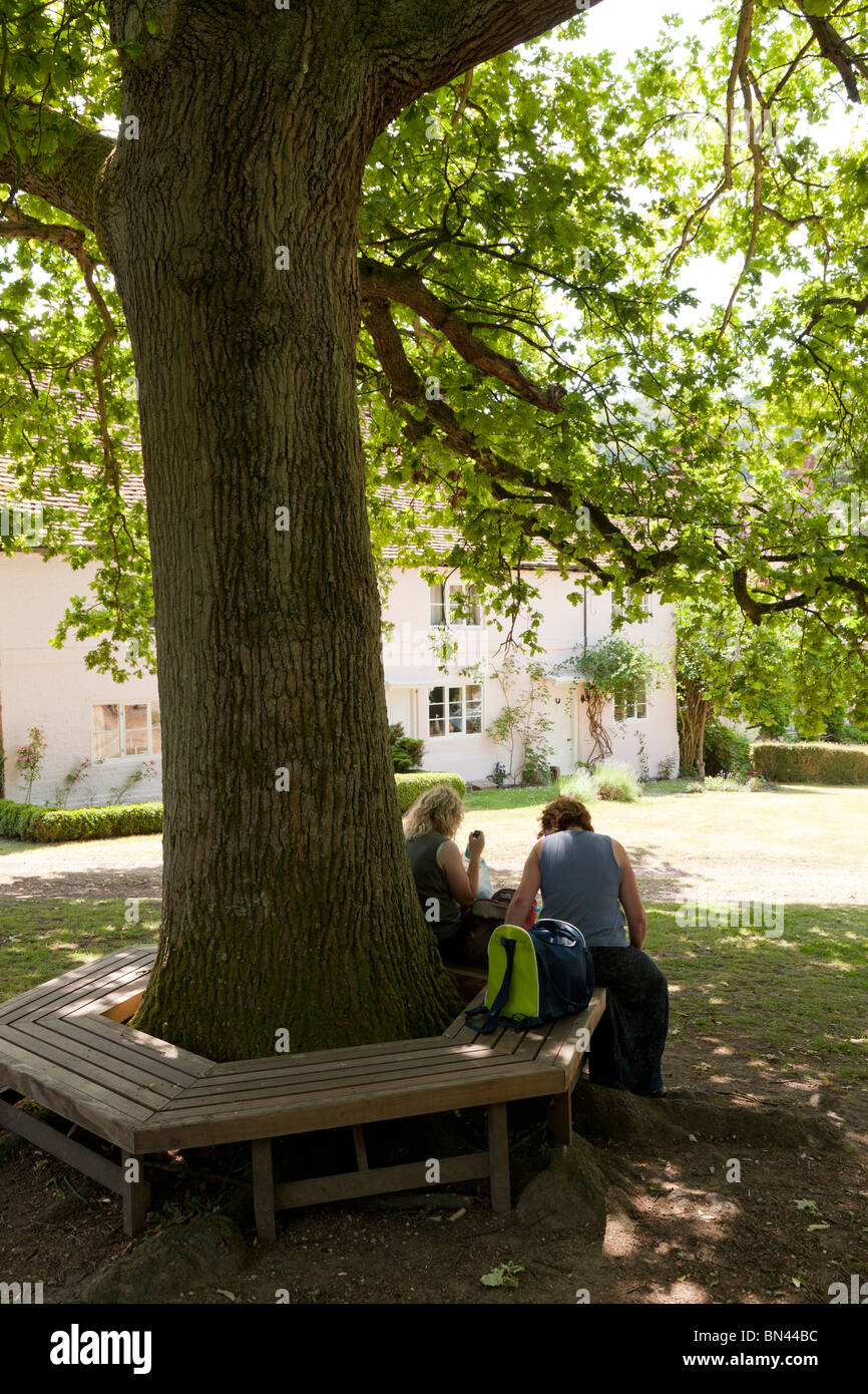 people resting on tree bench under the shade of an oak tree in Selborne outside the church Stock Photo