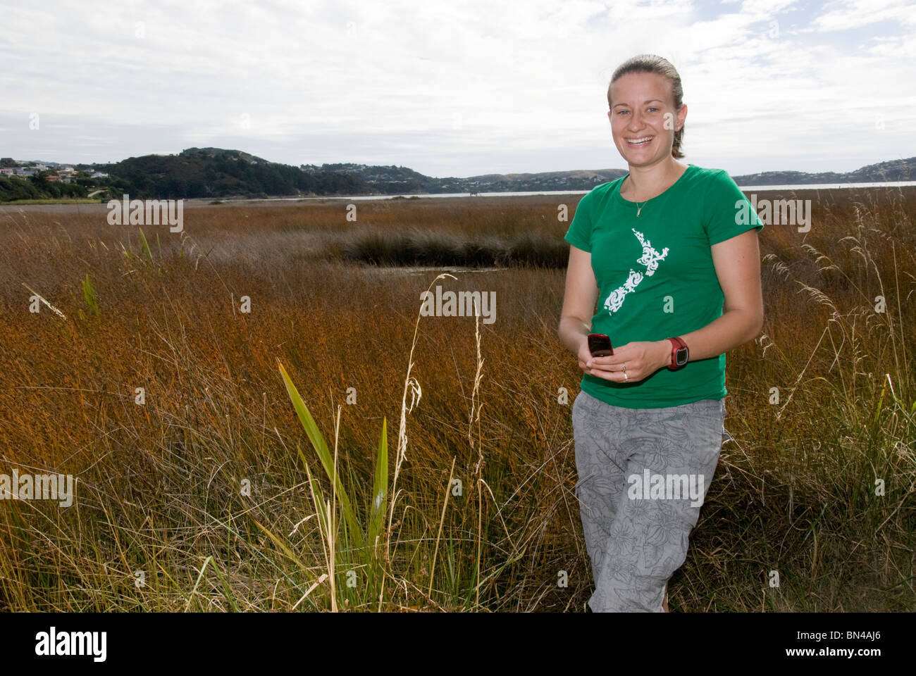 Young woman, 20's, in green New Zealand tee shirt at wildlife reserve, wetland, Pauatahanui Inlet, Wellington, North Island, Stock Photo