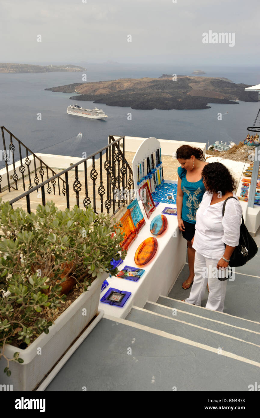 2 Tourists looking at Glass and ceramic Tourist Souvenirs in Santorini with a cruise  ship in the caldera on the horizon Stock Photo