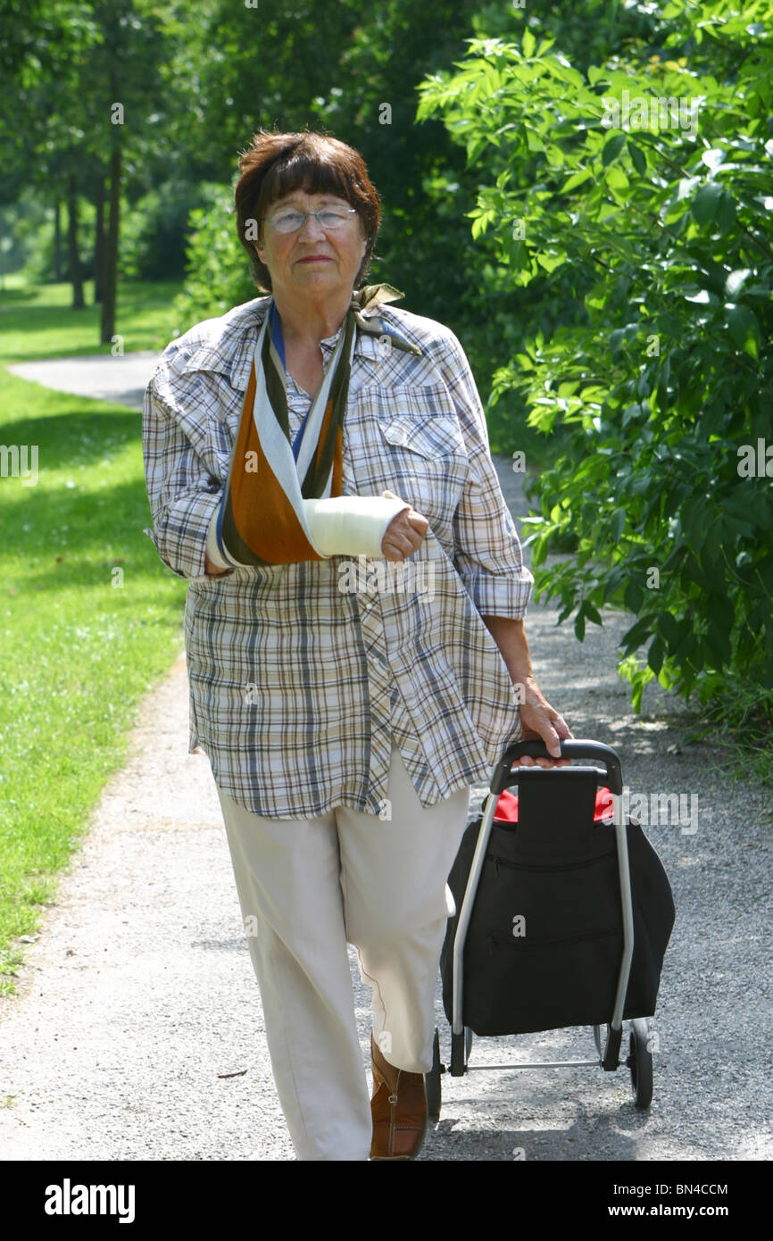 Elderly lady walking in the park with broken arm in sling Stock Photo