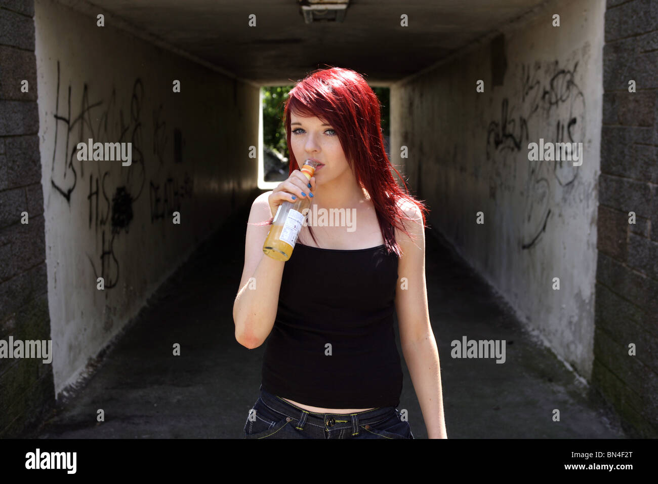 Teenage girl drinking a bottle of alcohol outside near a underpass. Stock Photo
