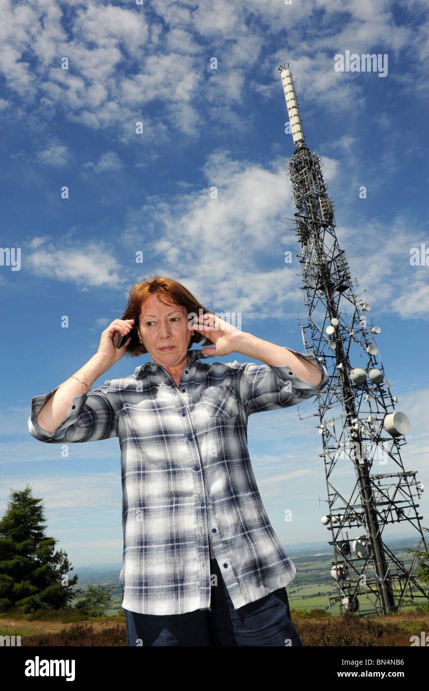 Woman using a mobile phone next to the The Wrekin transmitting station which is a telecommunications and broadcasting station Stock Photo