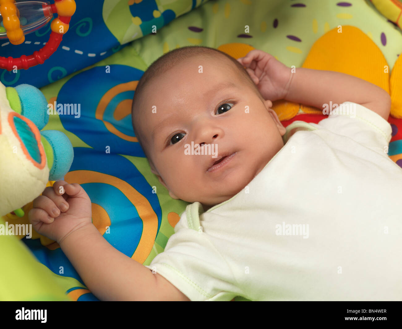Six week old cute baby boy lying in a colorful play mat with toys Stock