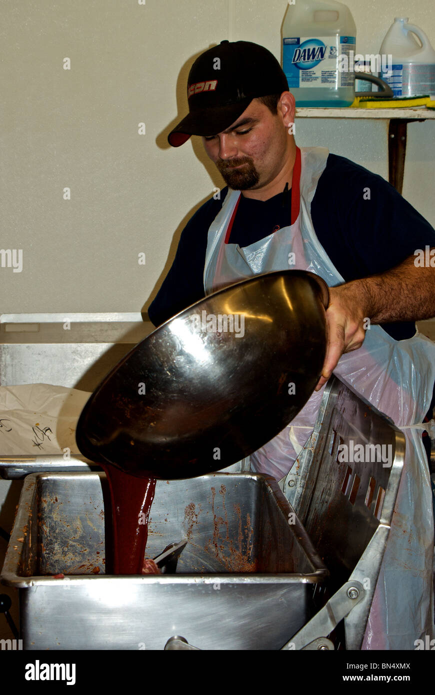Worker adding spice solution mixture to ground raw pork in mixer to make boudin sausage at The Sausage Link factory Sulphur LA Stock Photo