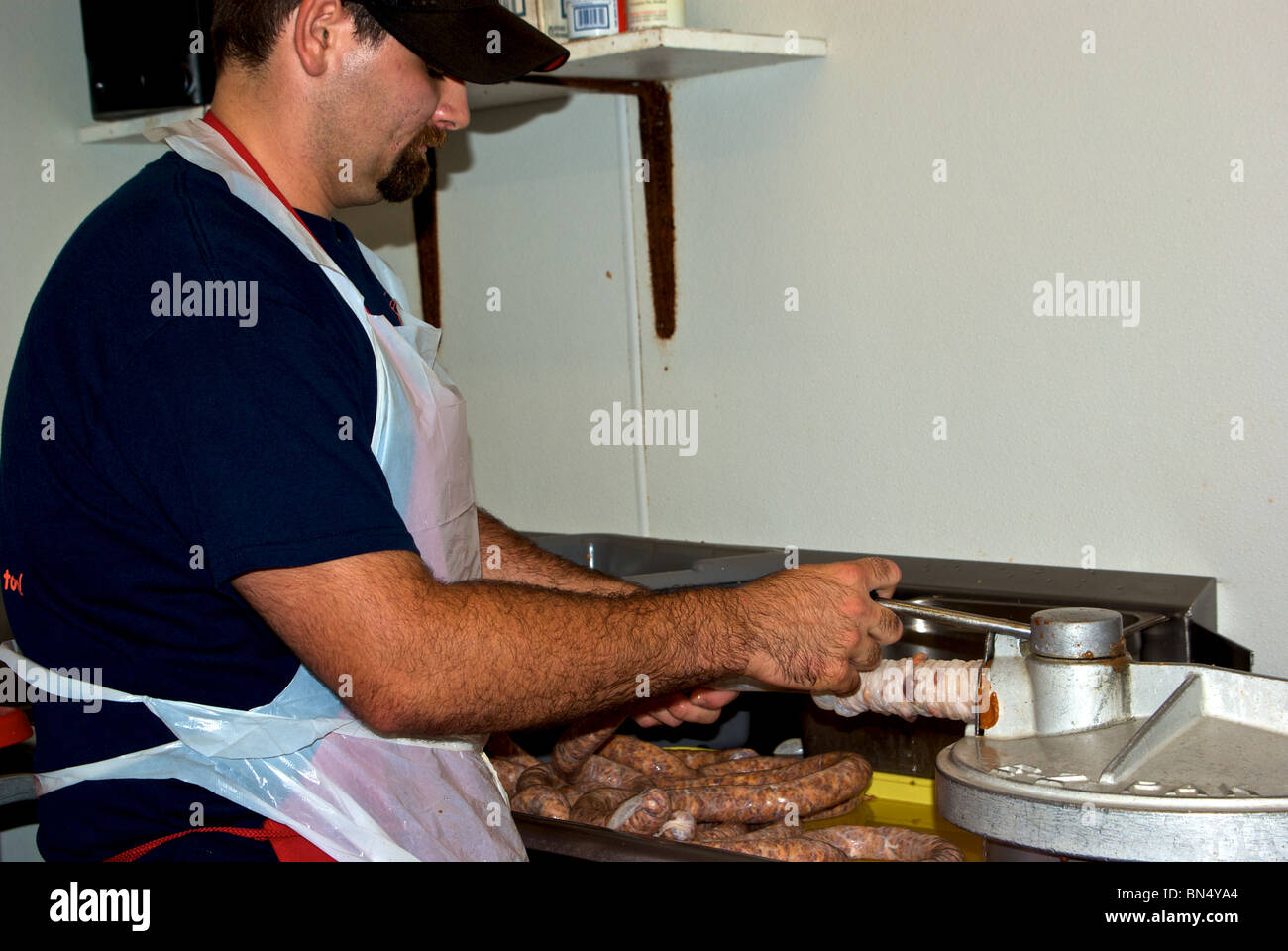 Worker extruding boudin pork sausages into natural gut casing from sausage maker at The Sausage Link factory Stock Photo