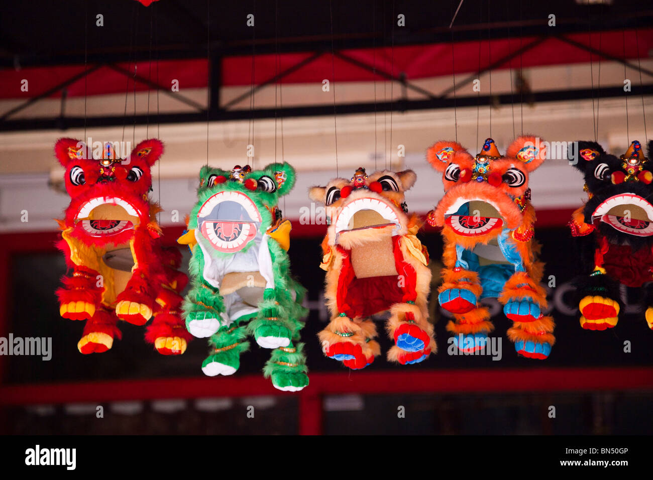 Chinese Lion dancing puppets hang from a storefront window in Singapore Stock Photo