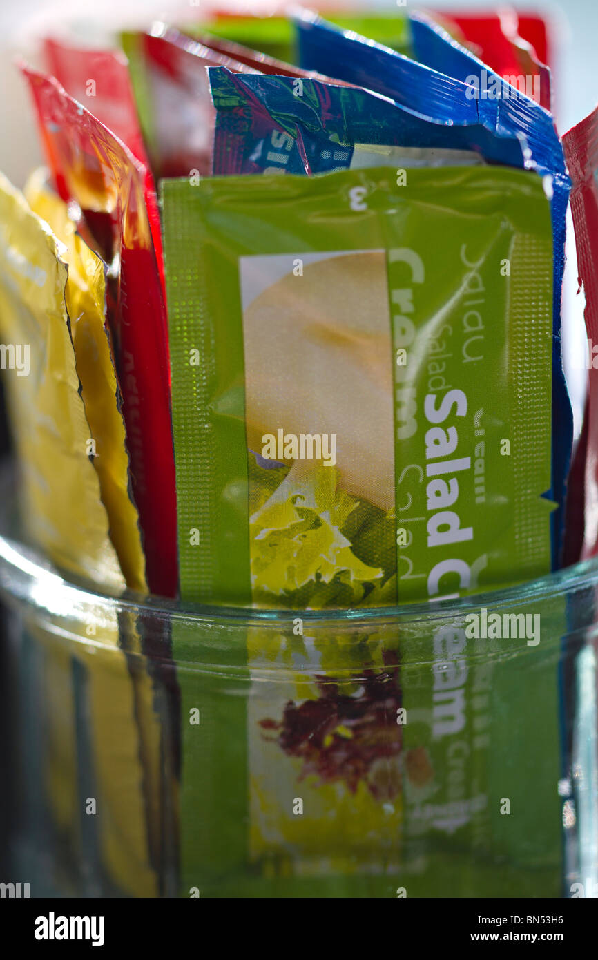 Sachets of salad cream and other condiments in a jar in a British cafe. Stock Photo
