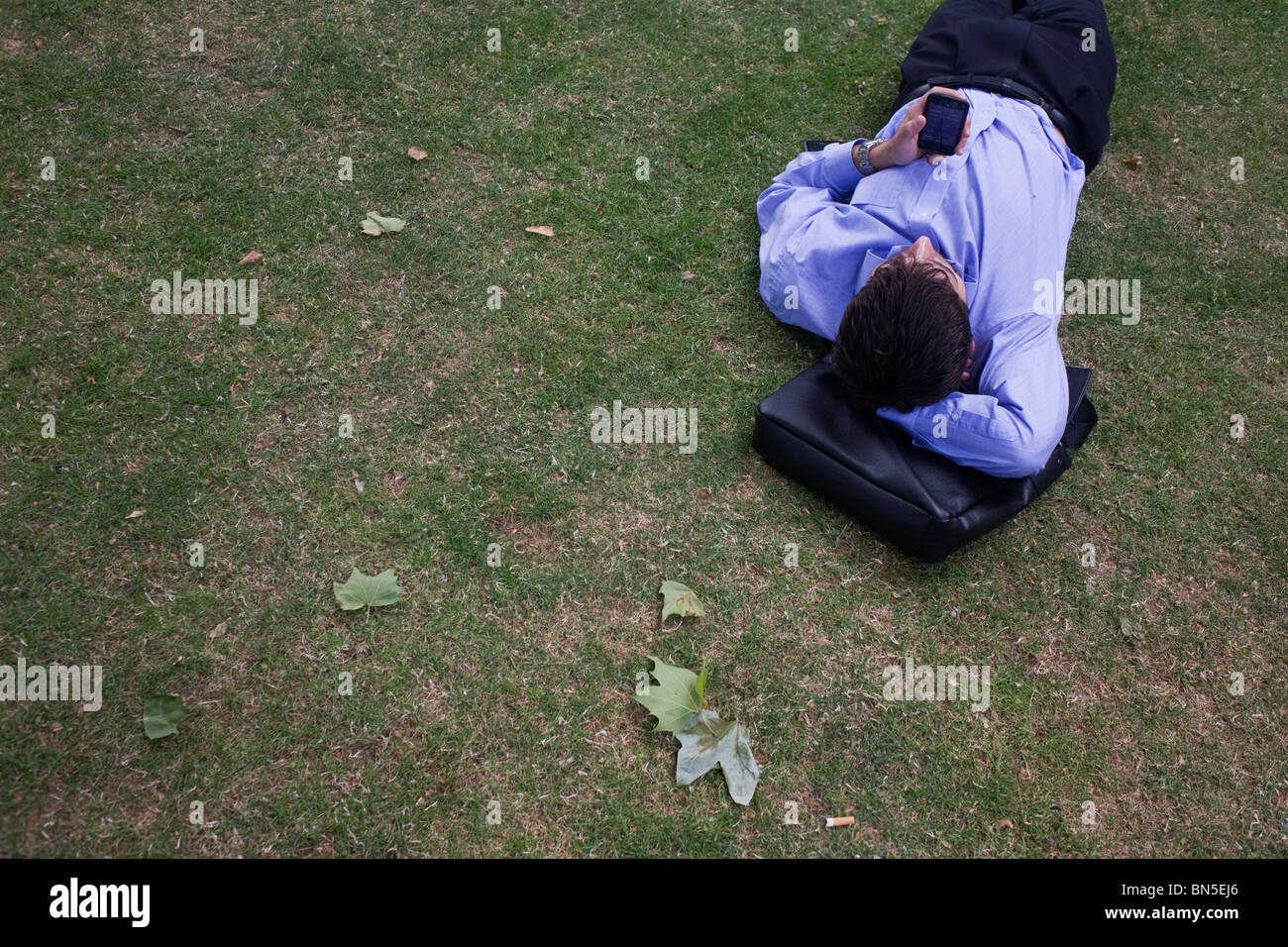 Young businessman fiddles with his touch pad iPhone during a lunchtime break on the grass in St. Paul's cathedral churchyard. Stock Photo