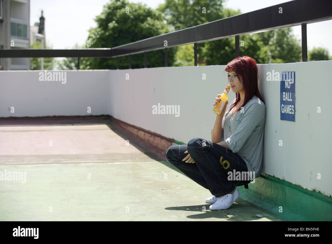 Teenage girl drinking alone in a town car park. Stock Photo