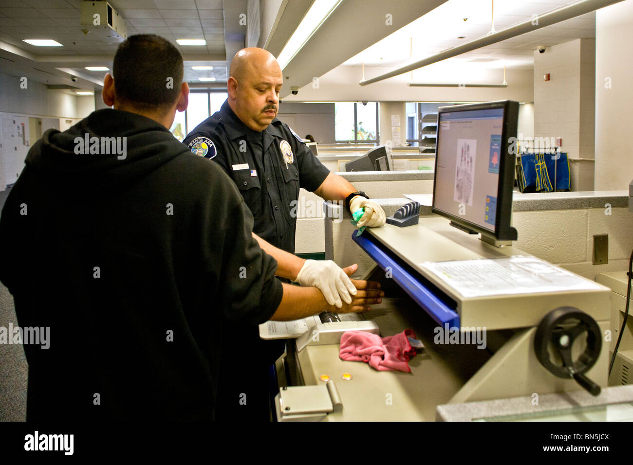 A uniformed Hispanic police officer takes an electronic palm print of a newly-arrested prisoner during booking. MODEL RELEASE. Stock Photo