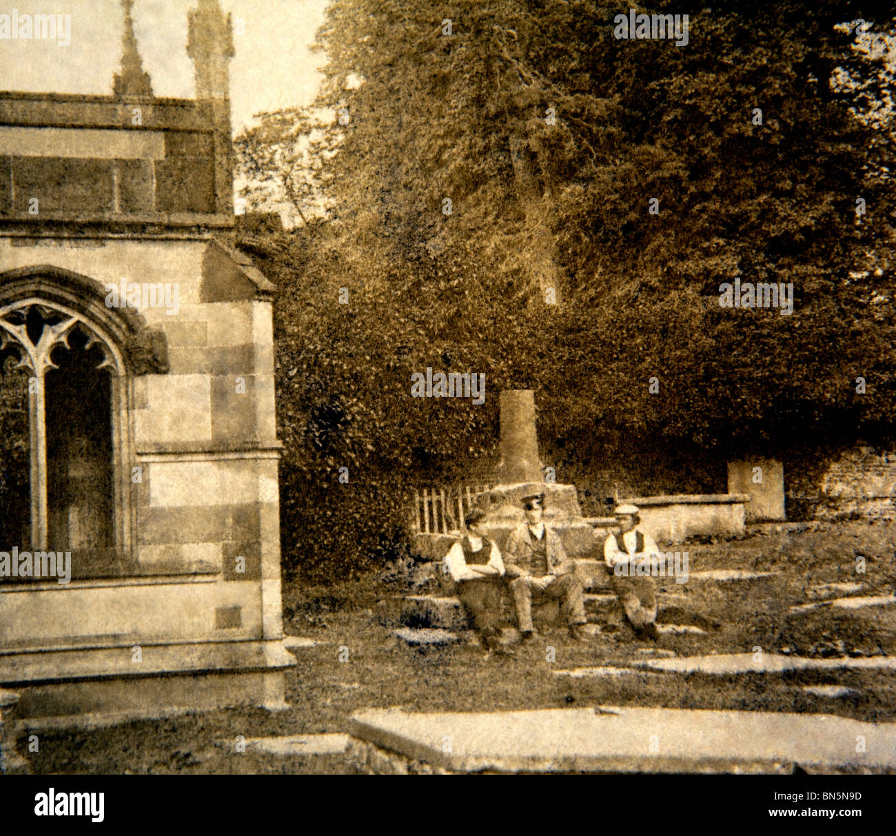 UK, England, Cheshire, Macclesfield, Victorian Gawsworth three men sitting on base of churchyard cross in 1860s Stock Photo