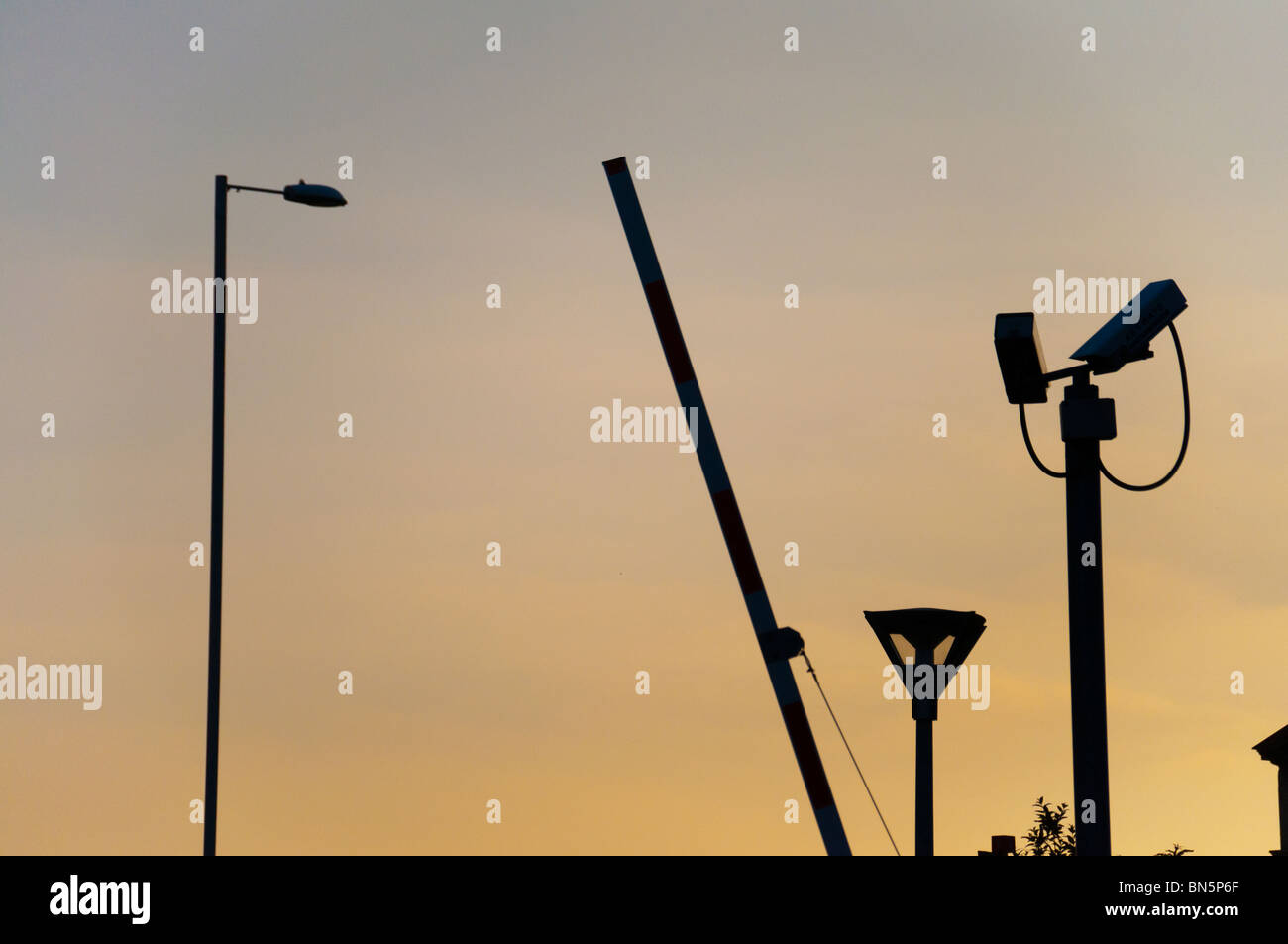 A CCTV camera, lamppost, light and car parking barrier all silhouetted