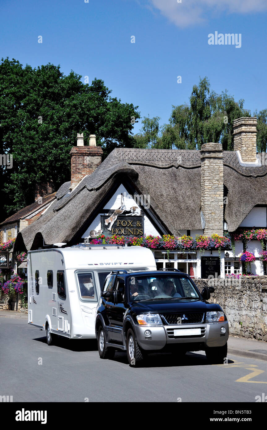 Car with caravan passing The Fox & Hounds Inn, Church Street, Bredon