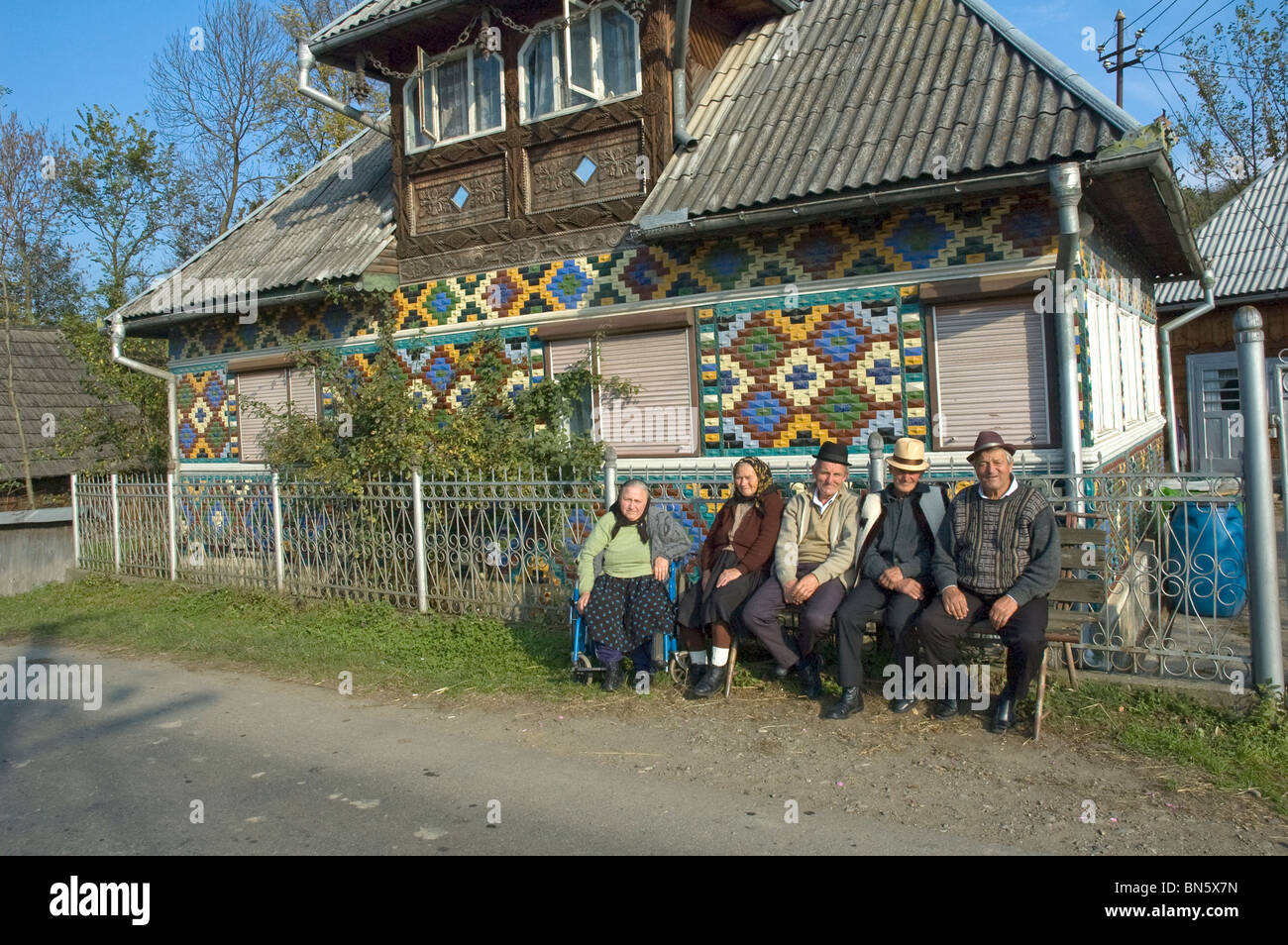 Elderly Romanians relax in the sushine outside in a  colourfully decorated village house Stock Photo