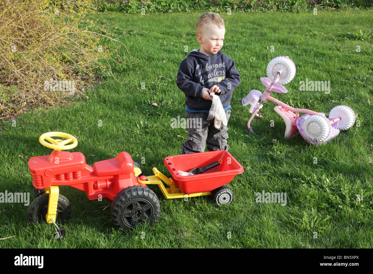 Toddler boy in the garden pretending to be a farmer with a tractor MODEL RELEASED Stock Photo