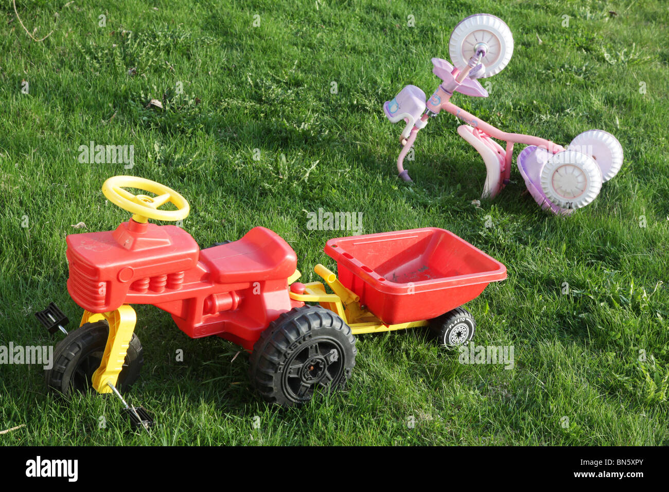 Plastic toys tractor tricycle abandoned in a family home garden by children when playtime is over Stock Photo