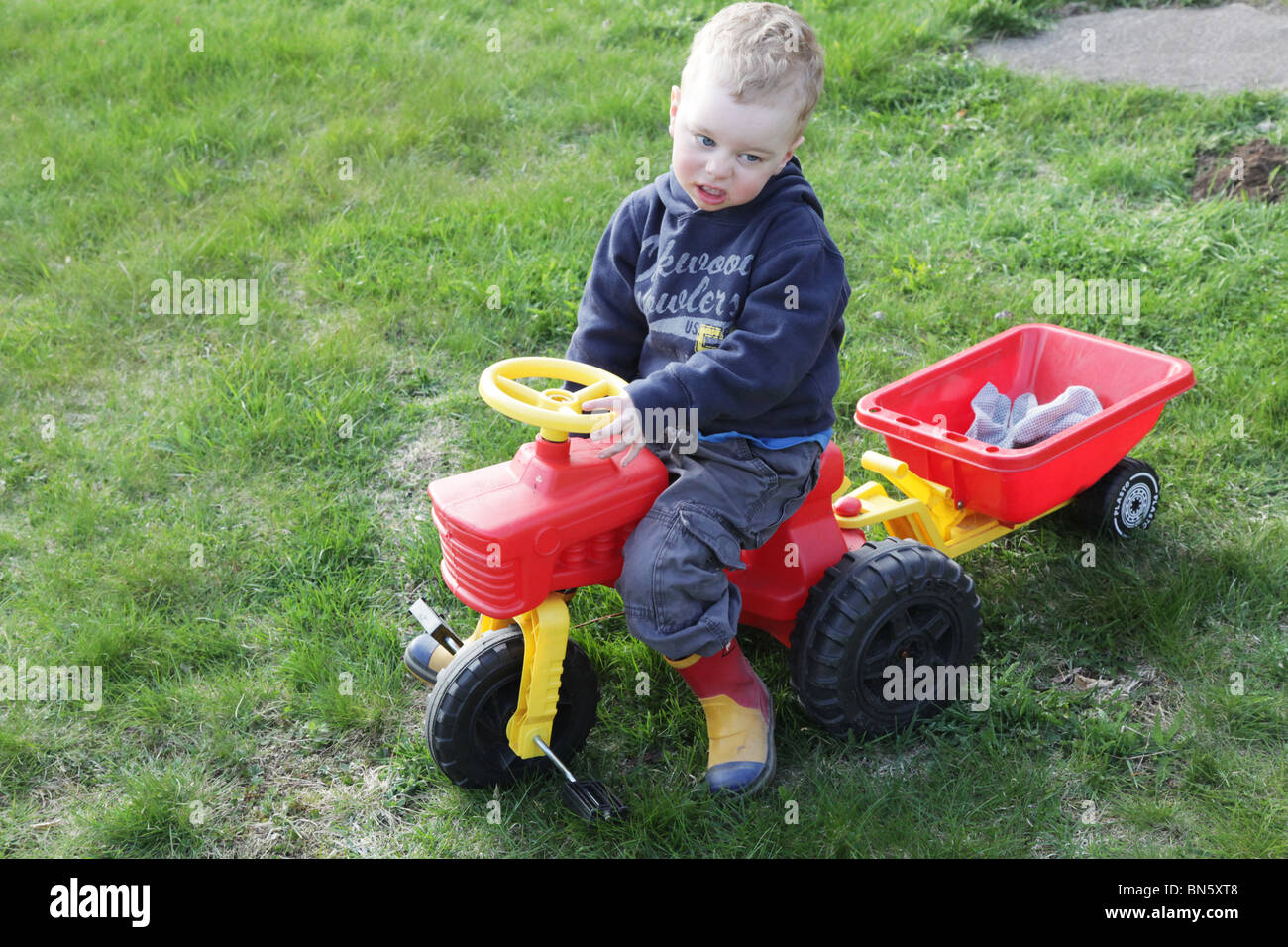 Toddler boy in the garden pretending to be a farmer driving a tractor MODEL RELEASED Stock Photo