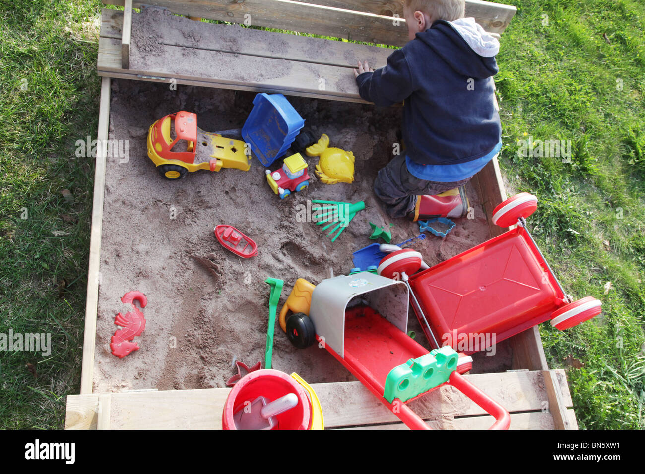 Toddler boy in the garden playing in a sandpit with plastic toys MODEL RELEASED Stock Photo