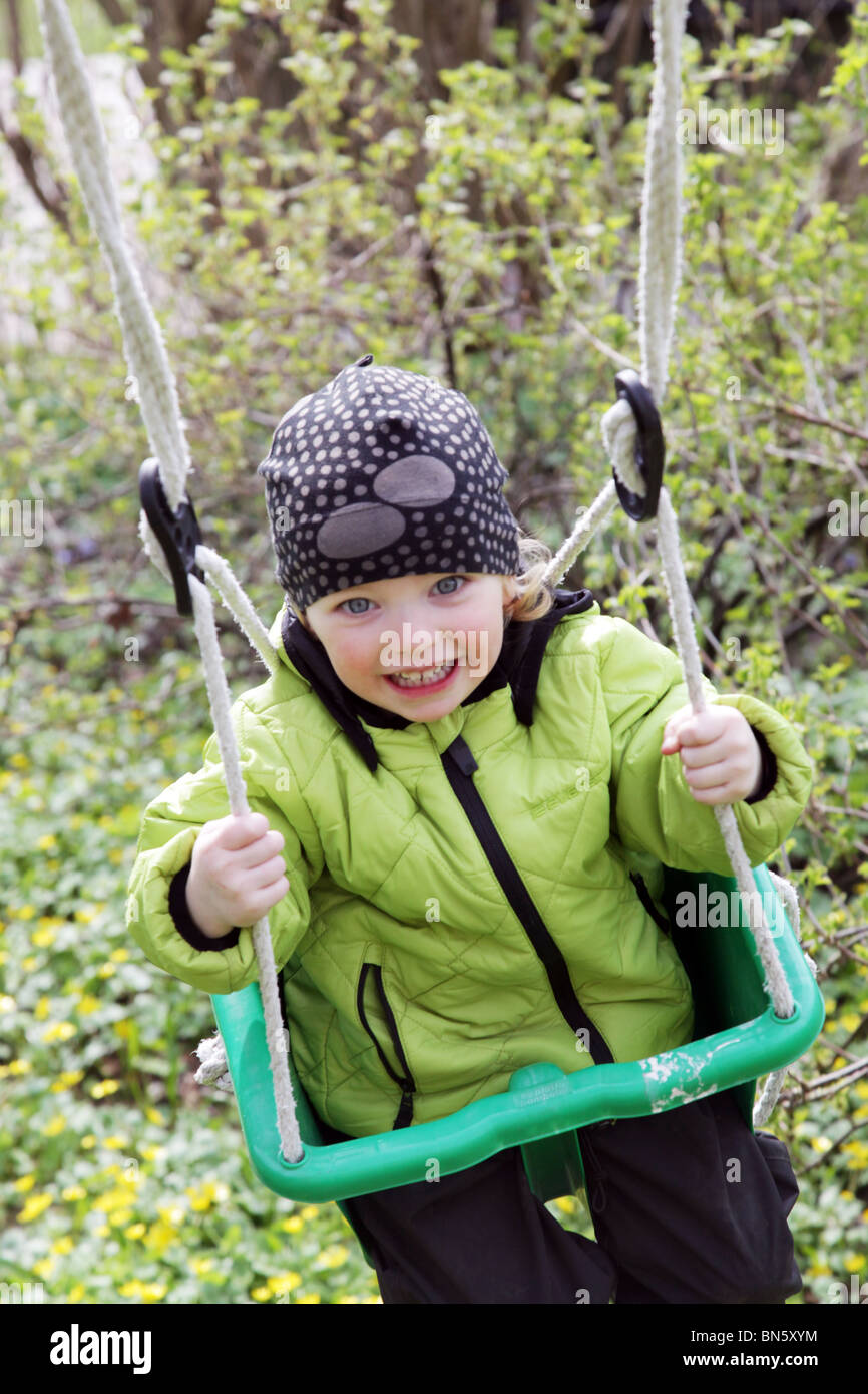 Toddler little girl having fun on a swing in a garden hanging from a tree MODEL RELEASED Stock Photo