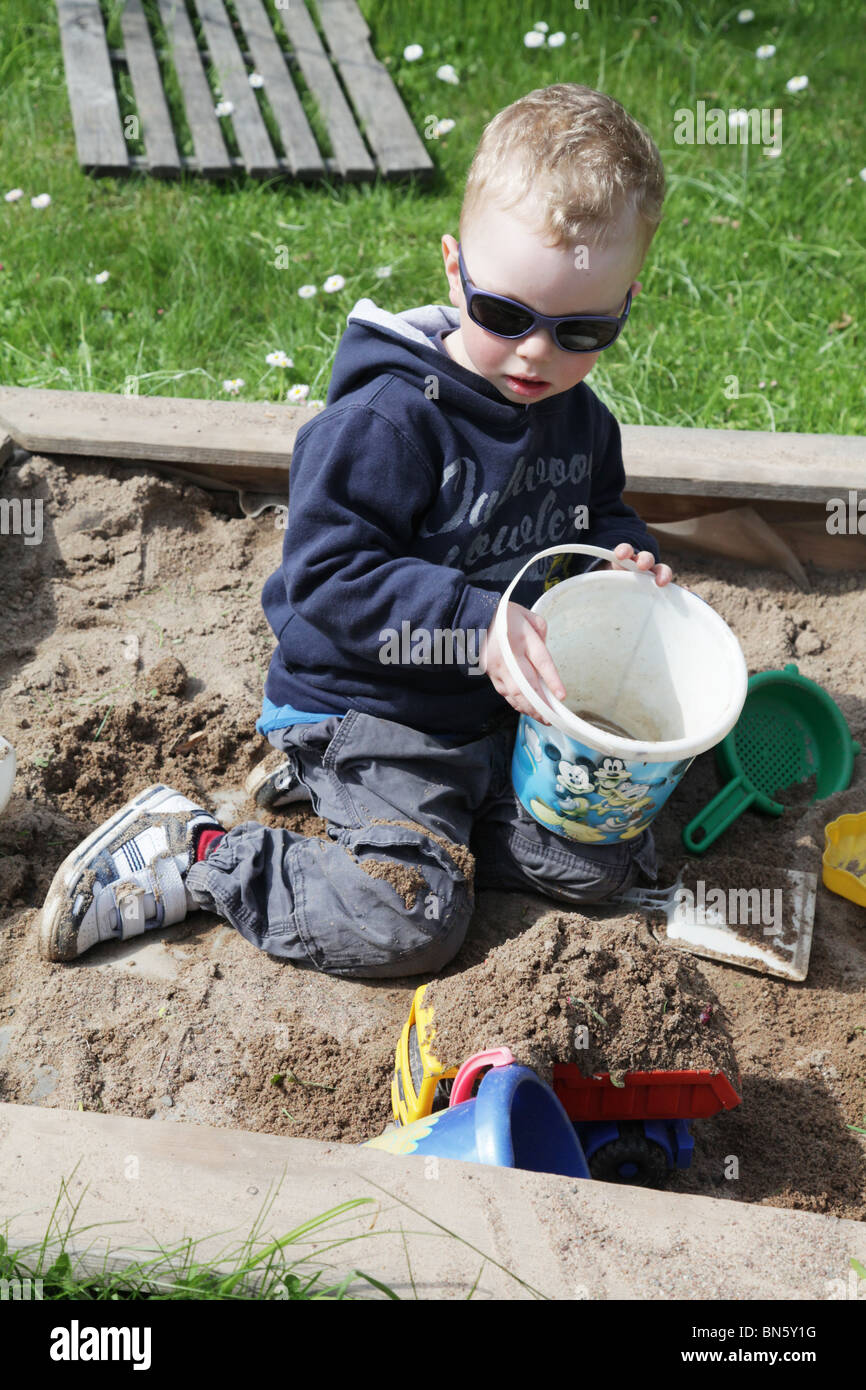 Toddler boy in the garden playing in a sandpit with plastic toys MODEL RELEASED Stock Photo