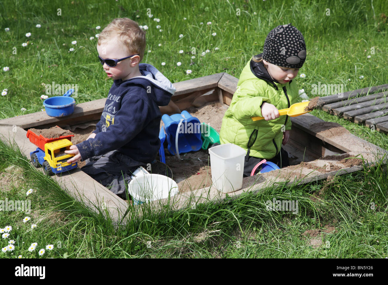Toddlers siblings boy girl brother sister in the garden playing in a sandpit with plastic toys MODEL RELEASED Stock Photo
