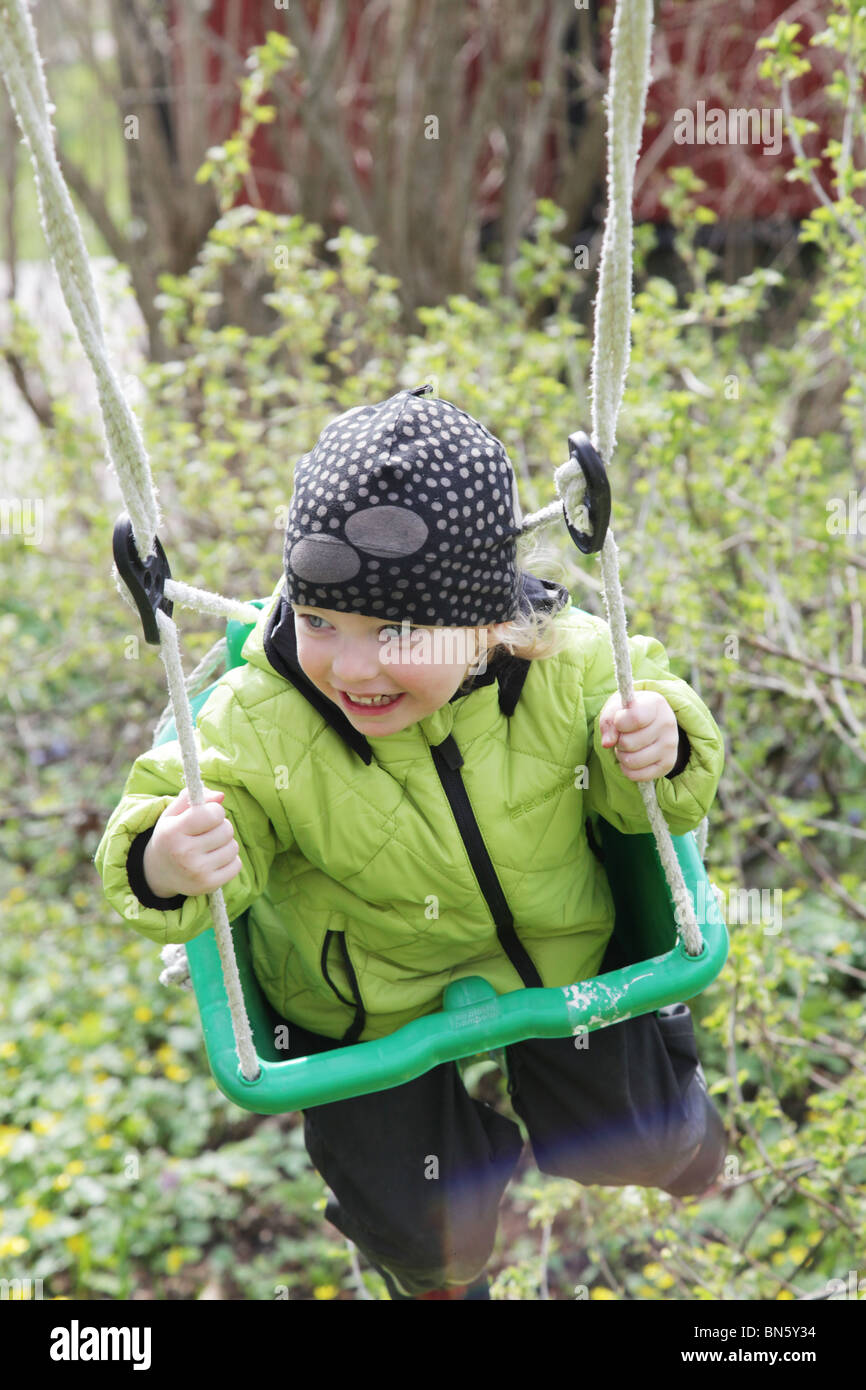 Toddler little girl having fun on a swing in a garden hanging from a tree MODEL RELEASED Stock Photo