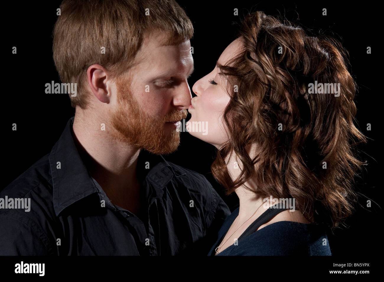 Serious couple in studio standing face to face, wife kissing husband’s nose Stock Photo